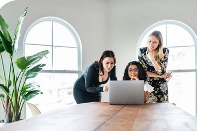 Foto von drei Frauen mit Blick auf einen Laptop in einem Besprechungsraum